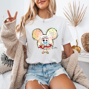Puede incluir: Camiseta blanca con un dibujo animado de Forky de Toy Story en una silueta de Mickey Mouse. El dibujo est&aacute; rodeado de salpicaduras de acuarela de colores y la palabra "Forky" est&aacute; escrita debajo del personaje.