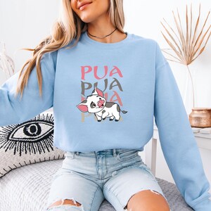 Puede incluir: Una sudadera azul claro con un cerdo de dibujos animados y la palabra "PUA" repetida tres veces en rosa, gris y marr&oacute;n.