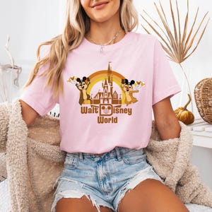 May include: A pink t-shirt with a graphic of Chip and Dale in front of the Walt Disney World castle. The graphic is in brown, orange, and yellow. The text "Walt Disney World" is below the graphic.