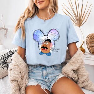 Puede incluir: Una camiseta azul claro con una imagen de dibujos animados de Mr. Potato Head con un sombrero azul y zapatos azules. La imagen est&aacute; dentro de una cabeza de Mickey Mouse azul, blanca y morada con fuegos artificiales. El texto "Mr. Potato Head" est&aacute; escrito debajo de la imagen.