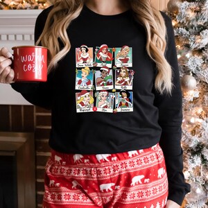 May include: Black long-sleeved shirt with a graphic of nine Disney princesses dressed in Christmas outfits. Each princess is in a separate frame with their name underneath. The names are: Snow White, Ariel, Aurora, Cinderella, Tiana, Belle, Rapunzel, Elsa, and Jasmine.
