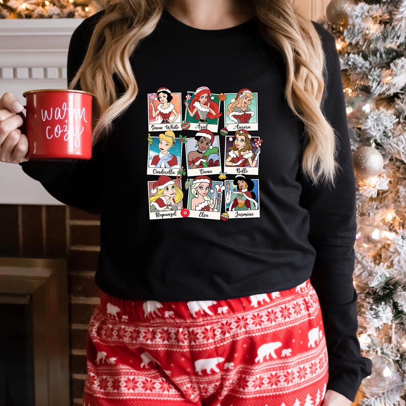 May include: Black long-sleeved shirt with a graphic of nine Disney princesses dressed in Christmas outfits. Each princess is in a separate frame with their name underneath. The names are: Snow White, Ariel, Aurora, Cinderella, Tiana, Belle, Rapunzel, Elsa, and Jasmine.