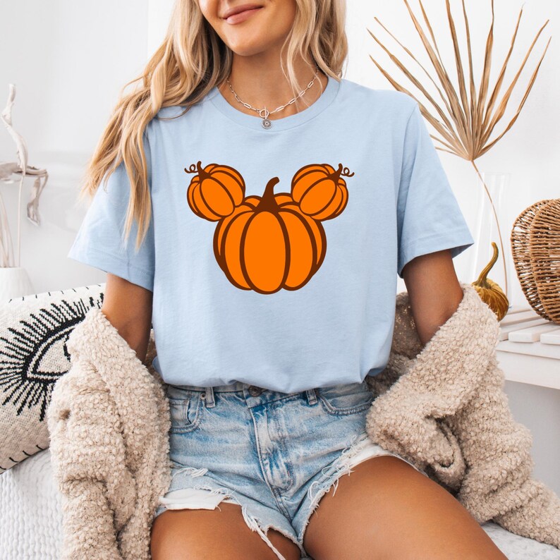 K&ouml;nnte beinhalten: Hellblaues T-Shirt mit einem K&uuml;rbisdesign in Form eines M&auml;usekopfes. Der K&uuml;rbis ist orange mit braunen Umrissen und Stielen. Das Shirt ist kurz&auml;rmlig und aus weichem Material. Ein grafisches T-Shirt zum Thema Herbst.
