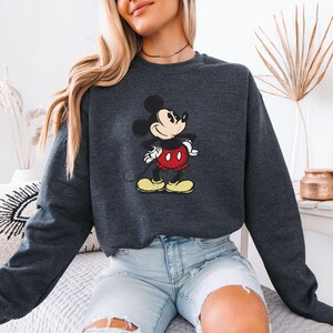 Puede incluir: Una sudadera gris oscuro con un gr&aacute;fico vintage de Mickey Mouse. La sudadera tiene mangas largas y cuello redondo.