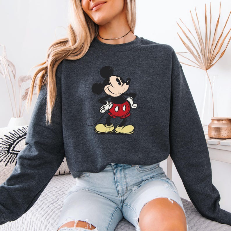 Puede incluir: Una sudadera gris oscuro con un gr&aacute;fico vintage de Mickey Mouse. La sudadera tiene mangas largas y cuello redondo.