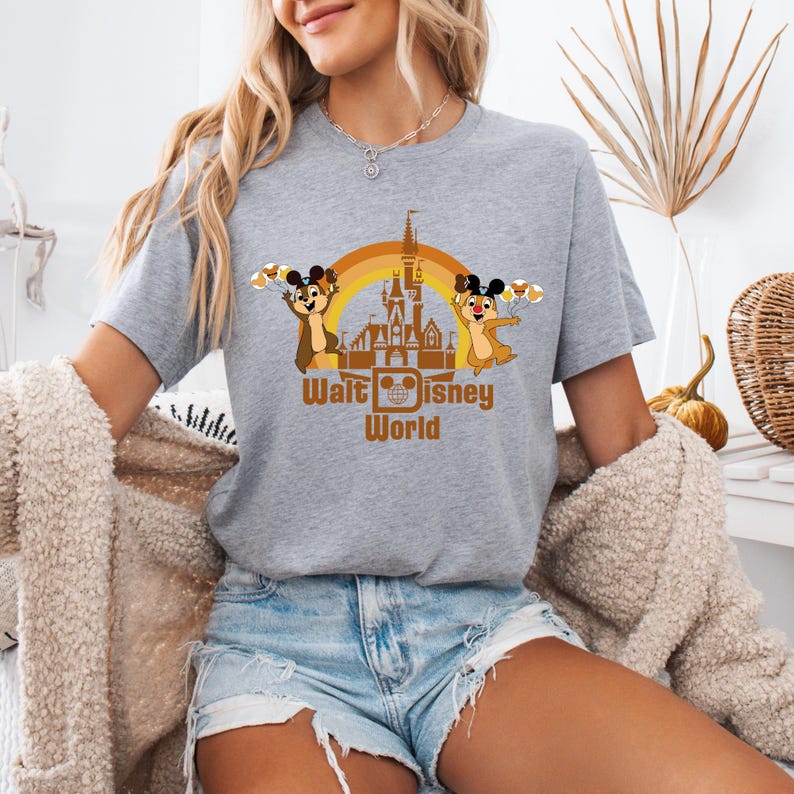 May include: A gray t-shirt with a graphic of Chip and Dale in front of the Cinderella Castle at Walt Disney World. The graphic includes a rainbow arch and the text "Walt Disney World".