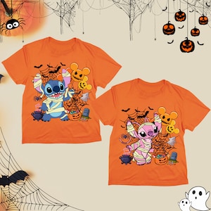 Puede incluir: Dos camisetas naranjas con tem&aacute;tica de Halloween con Stitch y Angel vestidos de momias. Las camisetas tienen un dise&ntilde;o de telara&ntilde;a con murci&eacute;lagos, calabazas y caramelos.