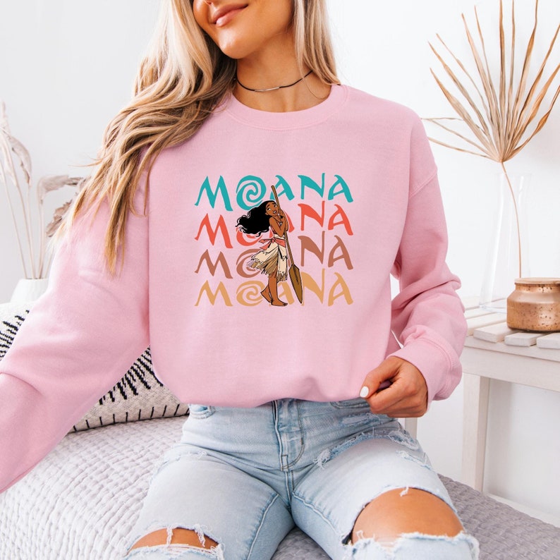 Puede incluir: Sudadera rosa con un gr&aacute;fico de Moana de la pel&iacute;cula de Disney Moana. El gr&aacute;fico se repite cuatro veces en un patr&oacute;n apilado, con cada iteraci&oacute;n ligeramente desplazada de la que est&aacute; arriba. El gr&aacute;fico es de estilo retro con una paleta de colores.