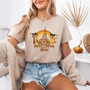 May include: A beige t-shirt with a retro-style graphic of Mickey Mouse and Chip 'n Dale in front of the Cinderella Castle at Walt Disney World. The graphic includes a rainbow arch and the text "Walt Disney World".