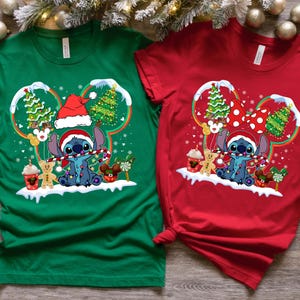 May include: A green t-shirt and a red t-shirt, each featuring a graphic of Stitch wearing a Santa hat and holding a candy cane. The design includes Mickey-shaped ears, Christmas trees, gingerbread cookies, and festive holiday decorations.