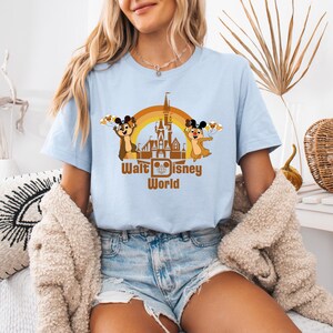 May include: A light blue t-shirt with a brown graphic of the Cinderella Castle at Walt Disney World. Two chipmunk characters are on either side of the castle, holding balloons. The text "Walt Disney World" is below the castle.