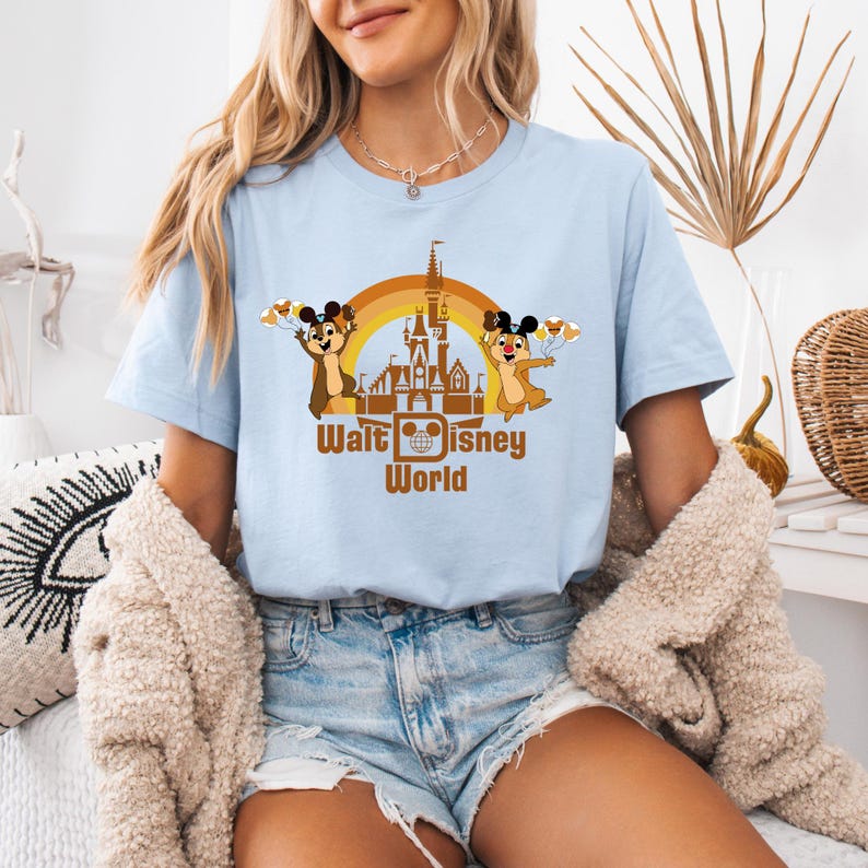 May include: A light blue t-shirt with a brown graphic of the Cinderella Castle at Walt Disney World. Two chipmunk characters are on either side of the castle, holding balloons. The text "Walt Disney World" is below the castle.