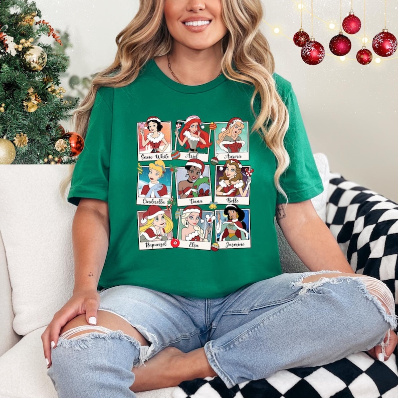 May include: Green t-shirt with a collage of nine Disney princesses dressed in Christmas outfits. Each princess is in a separate square with her name underneath. The princesses are Snow White, Ariel, Aurora, Cinderella, Tiana, Belle, Rapunzel, Elsa, and Jasmine.