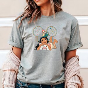 Może przedstawiać: Szary T-shirt z kresk&oacute;wkową postacią Moany z filmu Disneya Moana, z jej świnią Pua i kogutkiem Hei Hei. Obrazek znajduje się w sylwetce ucha Myszki Miki z fajerwerkami.