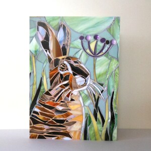 May include: A mosaic artwork depicting a brown and white rabbit in a green field with purple flowers. The rabbit is looking to the right and has long whiskers. The mosaic is made of small pieces of glass and tile.