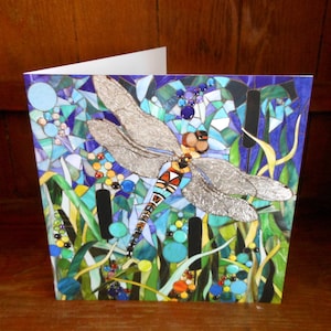 K&ouml;nnte beinhalten: Eine Gru&szlig;karte mit einer Libelle aus Mosaik mit silbernen Fl&uuml;geln, umgeben von blauen, gr&uuml;nen und gelben Mosaikdetails. Die Libelle ist vor einem Hintergrund aus blauem und violettem Mosaik platziert.