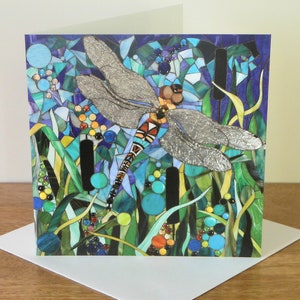 K&ouml;nnte beinhalten: Eine Gru&szlig;karte mit einer Mosaik-Libelle mit silbernen Fl&uuml;geln, umgeben von gr&uuml;nem und blauem Laub. Die Libelle ist scharf, der Hintergrund unscharf.