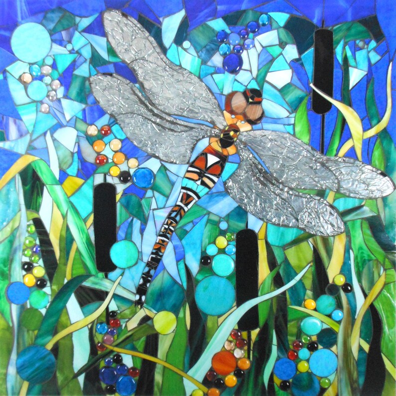 K&ouml;nnte beinhalten: Ein Mosaik-Kunstwerk, das eine Libelle mit silbernen Fl&uuml;geln vor einem blauen und gr&uuml;nen Hintergrund zeigt. Die Libelle ist von gr&uuml;nen Schilfpflanzen und blauen und gr&uuml;nen Glasperlen umgeben.