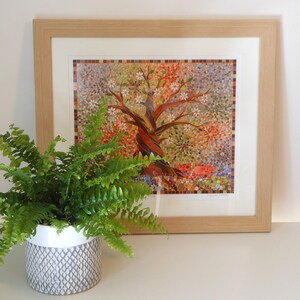 May include: A framed mosaic artwork depicting a colourful tree with white flowers. The artwork is displayed on a white surface next to a potted fern plant.