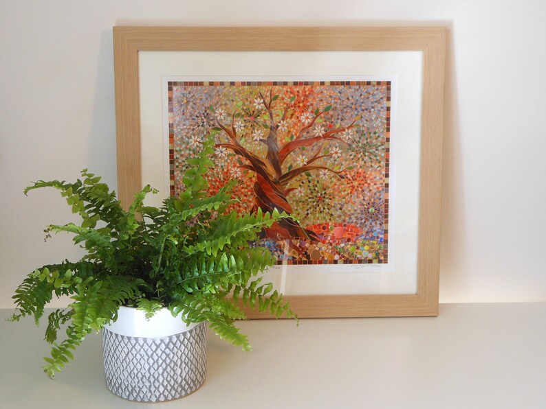 May include: A framed mosaic artwork depicting a colourful tree with white flowers. The artwork is displayed on a white surface next to a potted fern plant.