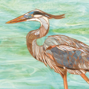 May include: A mosaic art piece depicting a blue heron with a long neck and beak, standing on a turquoise and green background.