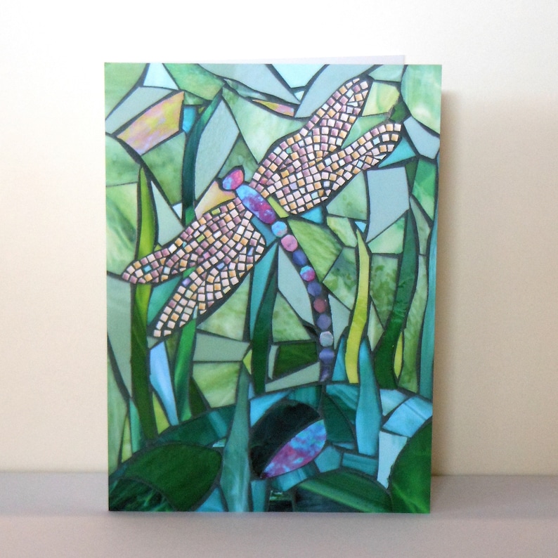 May include: A mosaic art piece depicting a dragonfly with pink, yellow, and blue accents, surrounded by green foliage.