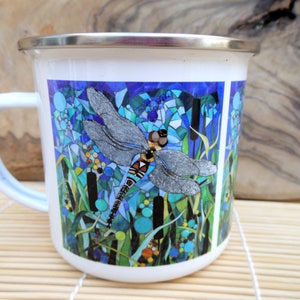 K&ouml;nnte beinhalten: Wei&szlig;e Emaille-Tasse mit einem bunten Mosaik-Design, das eine Libelle auf einem blauen und gr&uuml;nen Hintergrund zeigt.