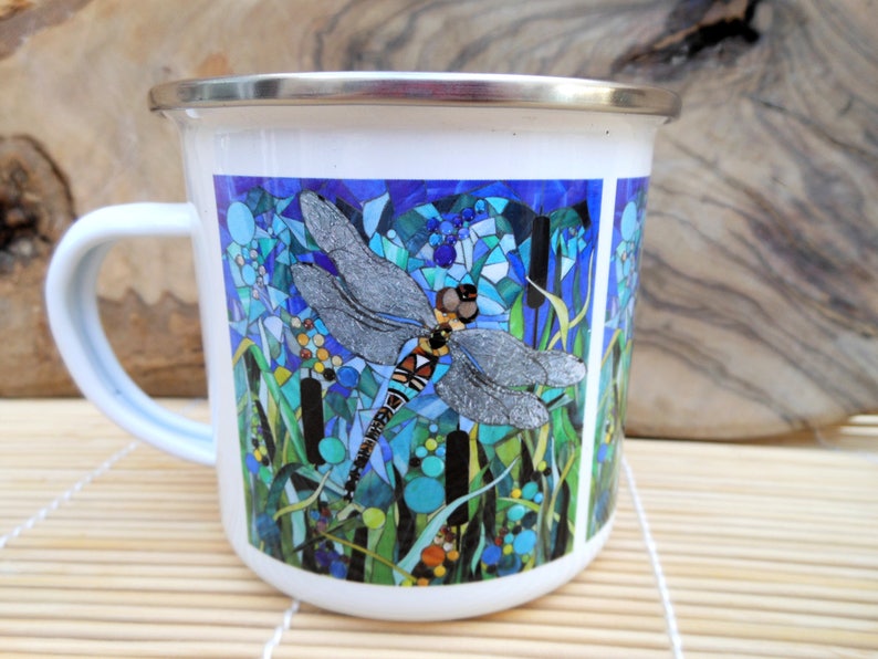 K&ouml;nnte beinhalten: Wei&szlig;e Emaille-Tasse mit einem bunten Mosaik-Design, das eine Libelle auf einem blauen und gr&uuml;nen Hintergrund zeigt.