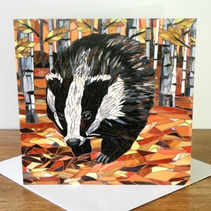 May include: A mosaic card featuring a badger in an autumnal forest setting. The badger is made of small, colorful tiles and is walking through a forest of birch trees. The background is a mix of orange, brown, and yellow tiles, representing fallen leaves.