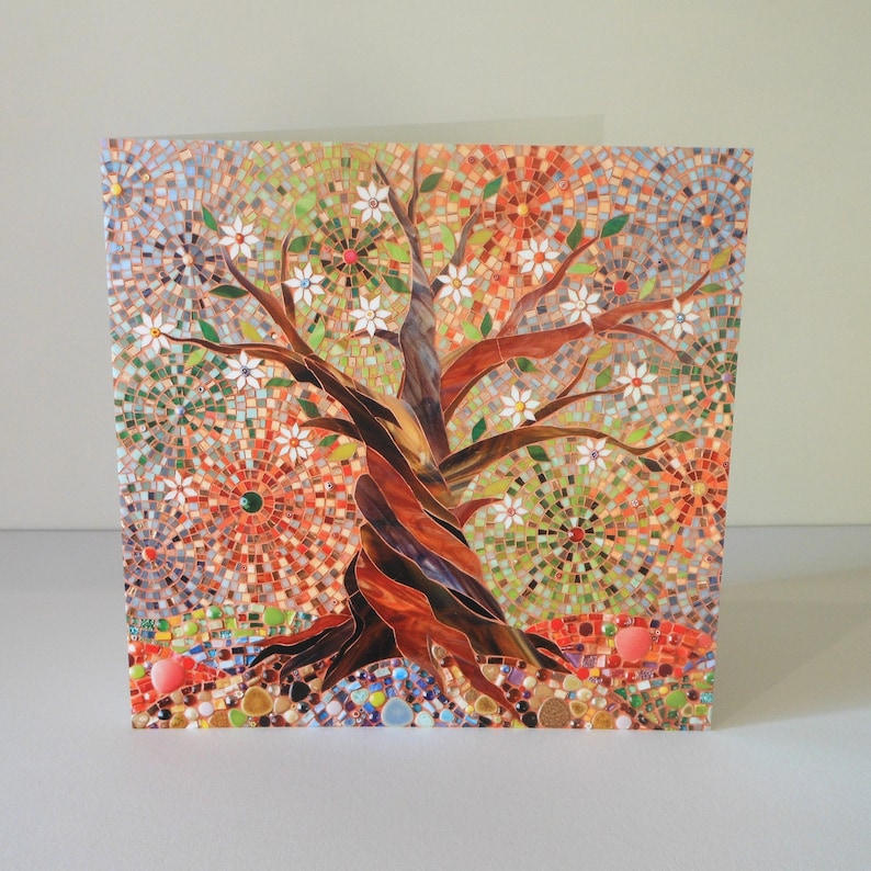 May include: A mosaic art card featuring a colourful tree with white flowers and a brown trunk. The background is a mix of red, orange, green, and blue mosaic tiles.