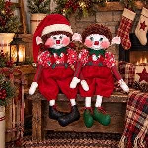 May include: Two plush elf dolls with white faces, rosy cheeks, and brown curly hair. The left elf wears a red hat with white trim, a red and white patterned shirt, and red pants with black shoes. The right elf wears a red and white patterned shirt, red pants, and green shoes.
