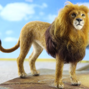 May include: A brown and tan lion with a long, dark brown mane. The lion is standing on a brown surface with a blue sky in the background.