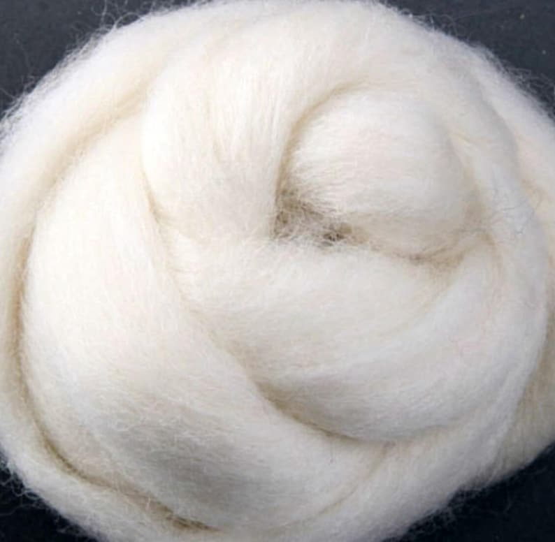 May include: A close-up of a white fluffy ball of wool fiber. The wool is soft and appears to be spun into a yarn.