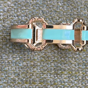 Peut inclure: Un bracelet en or avec un bandeau en émail bleu clair. Le bracelet a un design unique d'entrelacement.