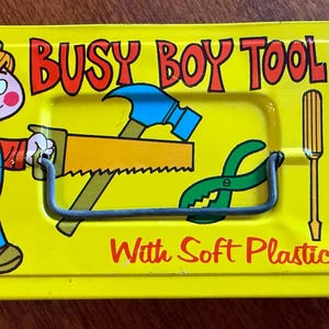 May include: Yellow metal tool chest with a cartoon boy holding a hammer. The chest has the words "Busy Boy Tool Chest" and "With Soft Plastic Tools" printed on it.