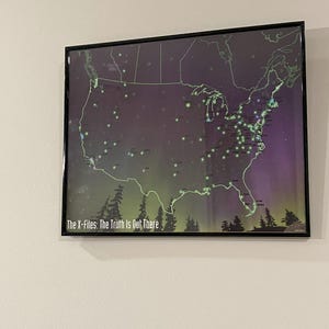 Pode incluir: Um mapa emoldurado dos Estados Unidos com luzes verdes que representam as localizações dos episódios de Arquivo X. O mapa tem um fundo roxo escuro e azul com uma moldura preta. O texto "The X-Files: The Truth Is Out There" está na parte inferior do mapa.