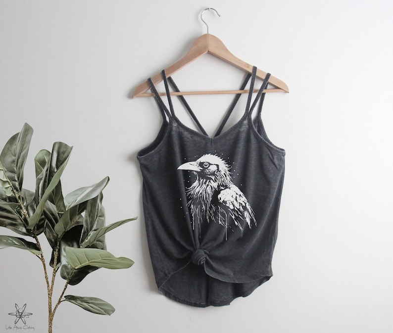 May include: A charcoal gray tank top with a white graphic of a raven. The tank top has a criss-cross strap design.