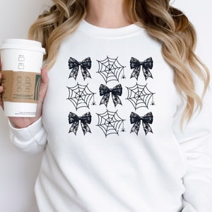 Puede incluir: Sudadera blanca con un patr&oacute;n blanco y negro de lazos y telara&ntilde;as.