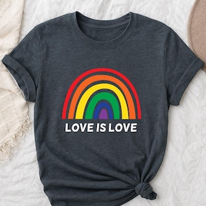 May include: Dark gray t-shirt featuring a rainbow design in red, orange, yellow, green, and purple. The text "LOVE IS LOVE" is printed in white below the rainbow. The shirt is made of a soft material.