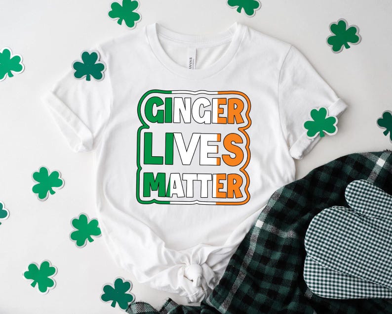May include: White t-shirt with a green, white, and orange graphic that says "Ginger Lives Matter". The graphic is in the style of the Irish flag. The shirt is surrounded by green shamrocks.
