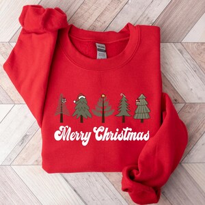 May include: Red Christmas sweatshirt with a white graphic of five stylized Christmas trees and the text "Merry Christmas".