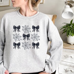 Puede incluir: Una sudadera gris con un dise&ntilde;o en blanco y negro de telara&ntilde;as y lazos. El dise&ntilde;o se repite en la parte delantera de la sudadera.