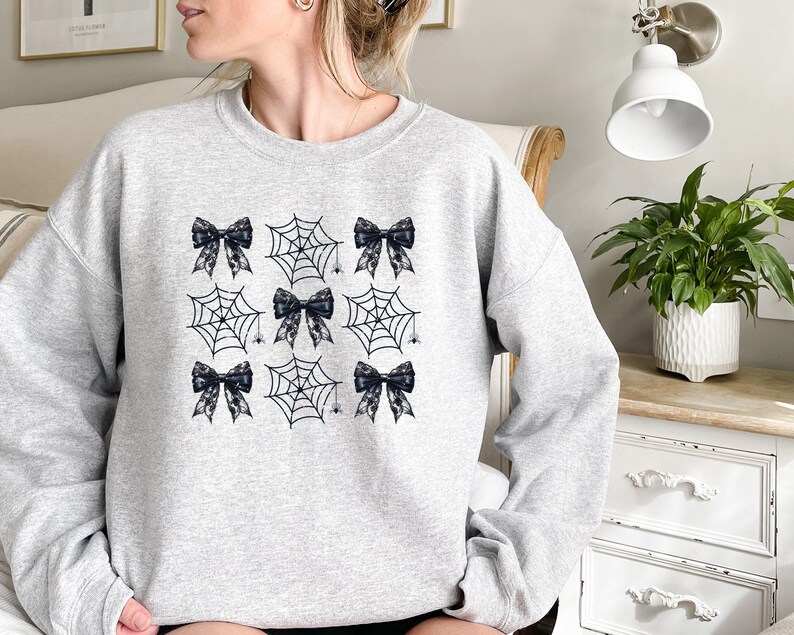 Puede incluir: Una sudadera gris con un dise&ntilde;o en blanco y negro de telara&ntilde;as y lazos. El dise&ntilde;o se repite en la parte delantera de la sudadera.