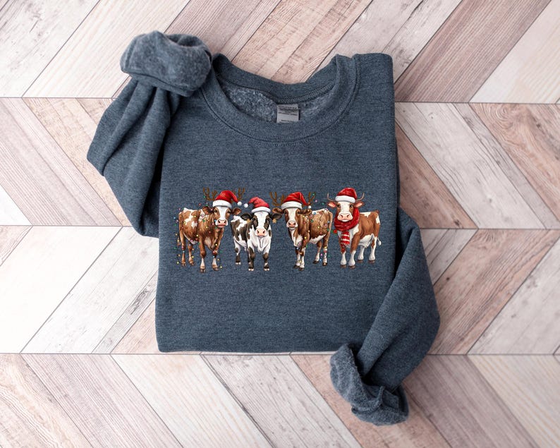 May include: A dark blue sweatshirt with a festive design of five cows wearing Santa hats. The cows are brown and white with red and white Santa hats.