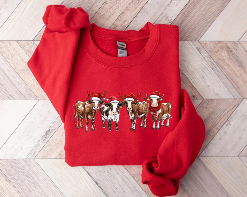 May include: Red Christmas sweatshirt with a graphic of five cows wearing Santa hats. The cows are brown and white with black noses and hooves.