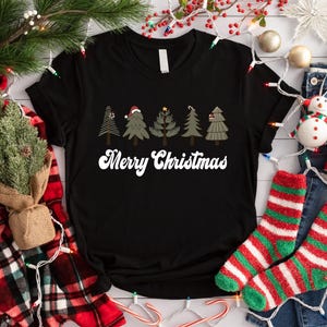 May include: Black t-shirt with a white "Merry Christmas" graphic and five stylized Christmas trees with red and green accents.