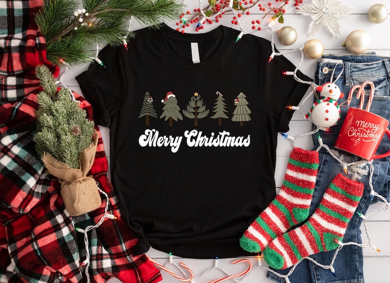 May include: Black t-shirt with a white "Merry Christmas" graphic and five stylized Christmas trees with red and green accents.