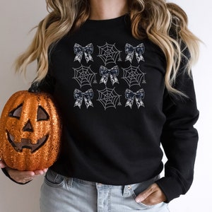Puede incluir: Sudadera negra con un dise&ntilde;o de telara&ntilde;a blanca y lazo negro.