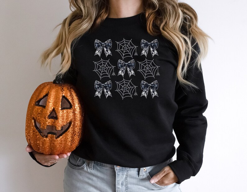 Puede incluir: Sudadera negra con un dise&ntilde;o de telara&ntilde;a blanca y lazo negro.
