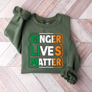 May include: Green sweatshirt with the text "Ginger Lives Matter" in white and orange letters inside a green, white, and orange rectangle.